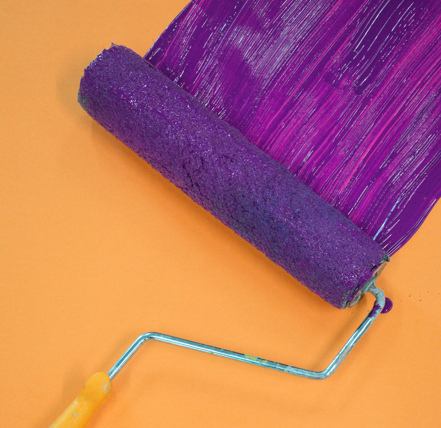 A brush painting an orange wall purple.