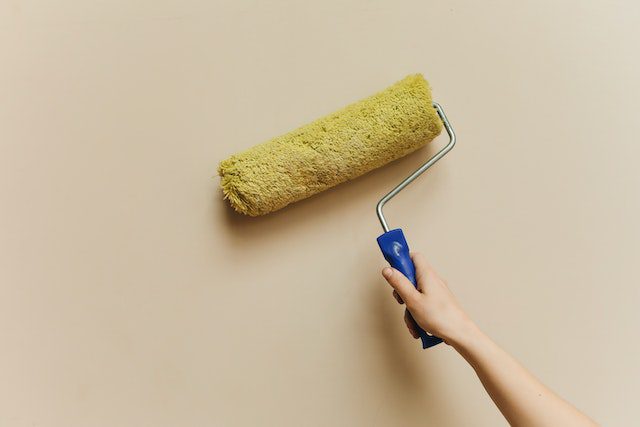 Person painting a wall using a yellow roller