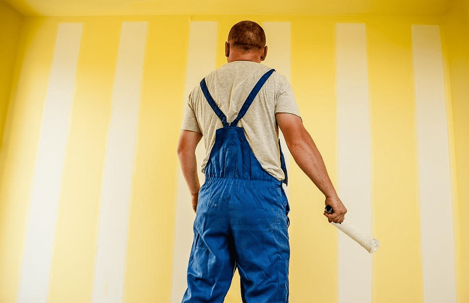 A building painter painting a wall in yellow strips