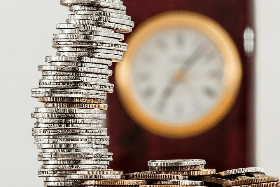 A stack of silver coins before a clock