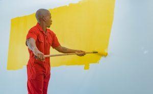 Professional painter in a red uniform painting a white wall yellow