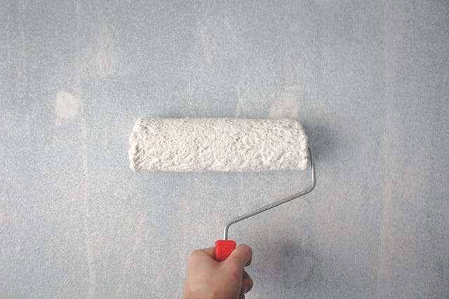 A painter using a roller brush on a wall.
